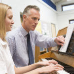 Teacher instructing adult student on playing the piano